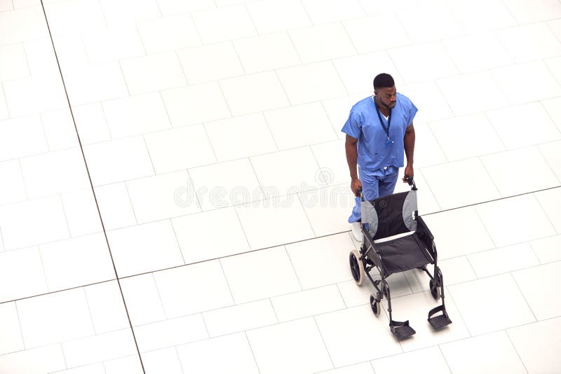Overhead View Of Male Nurse Pushing Empty Wheelchair Through Lobby Of Modern Hospital Building stock images